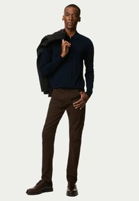 Marineblå strikpullover med lynlås krave, brune chinos og mørkebrune lædersko. Jakken hænger over skulderen og viser en slim fit.