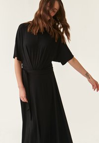 Schwarzes Maxikleid aus einem weichen, fließenden Stoff. Mit kurzen Ärmeln, einem Wickeldesign mit einem Knoten vorne und einer lockeren Passform.