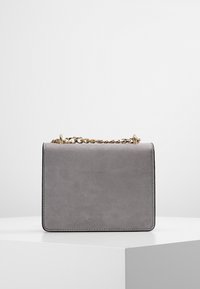 Borsa in finta suede grigia con forma rettangolare, tracolla in catena dorata e dettagli cuciti lungo i bordi. Texture liscia, design minimale.