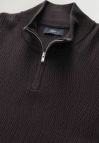 Donkerpaarse zip-necksweater met ribbeltextuur en verticale streepjespatroon. Zilveren ritsdetail bij de halslijn. Merktag zichtbaar.