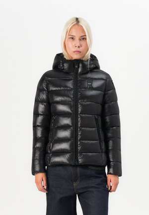 Black puffer jacket with a hood, featuring quilted panels, glossy texture, front zipper, and side pockets. Styled with dark jeans.