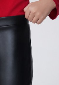 Černá sukně z umělé kůže s hladkou texturou a přiléhavým designem, s vysokým pasem a detailním prošíváním podél švů.