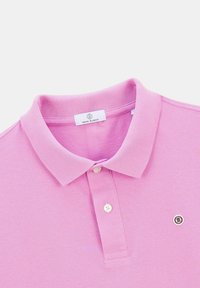 Polo rose clair avec un col, deux boutons au cou et un petit logo sur le côté gauche. Étiquette en texte visible à l'intérieur du col.