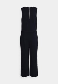 Svart ärmlös byxdress med dragkedja bak, vida ben, slät tyg och subtila accentringar i midjan.