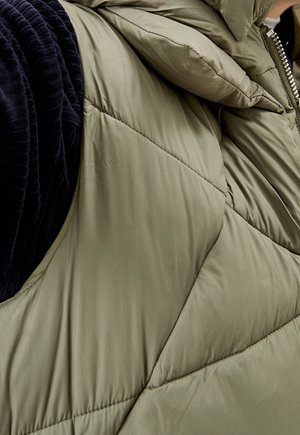 Gilet imbottito verde oliva con motivo trapuntato e colletto alto, con dettagli in velluto a coste neri sulle maniche. Chiusura con zip visibile.