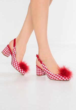 Czerwono-białe sandały na obcasie w kratkę, z blokowym obcasem i czerwonymi puszystymi pomponami na palcach, noszone na gołych stopach na białym tle.