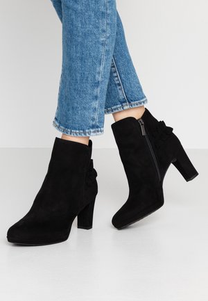 Bottines en daim noir avec une fermeture éclair sur le côté, un talon courbé et un détail froncé à l'arrière. Le matériau texturé offre une apparence douce.