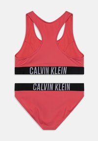 Calvin Klein kupaći kostim u vibrantnoj koralj crvenoj boji. Sadrži majicu s racerback dizajnom i odgovarajuće gaćice s crnim pojasom s logom. Glatka tekstura, rastezljivi materijal.