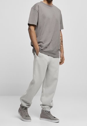 Hombre vistiendo una camiseta gris de manga corta y holgada, pantalones jogger gris claro y zapatillas altas grises, de pie con las manos en los bolsillos.