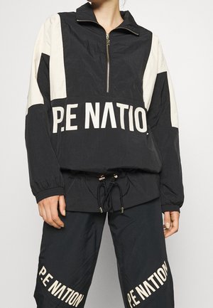 Sort vindjakke med beige detaljer, halv-zip foran, elastiske manchetter og justerbar snor i kanten, der har stort "P.E NATION" tryk.