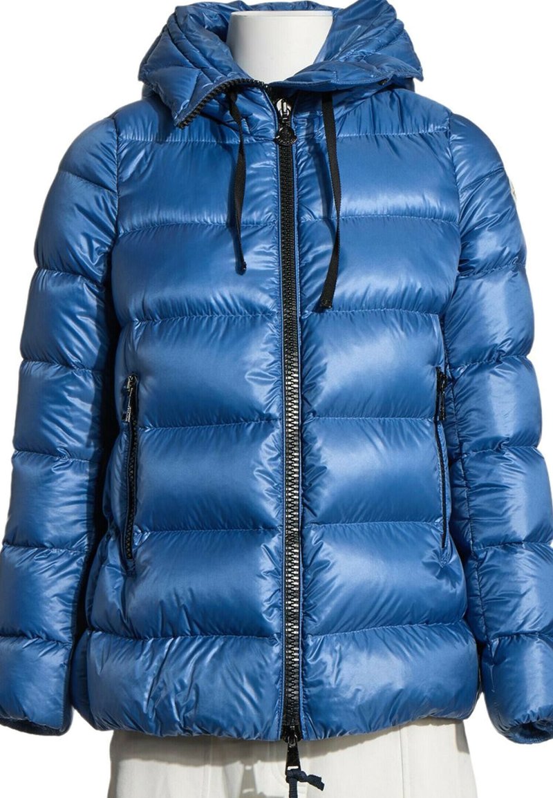 Doudoune bleu brillant avec capuche, fermeture éclair noire et cordons, et poches latérales zippées sur un torse de mannequin blanc.