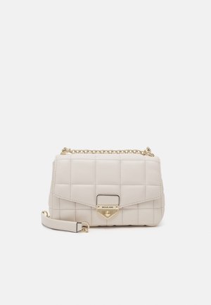 Beżowa pikowana skórzana torebka na ramię ze złotym łańcuszkiem i przednim zapięciem z wygrawerowanym logo "Michael Kors" na białym tle.