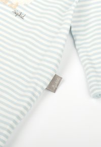 Chemise à manches longues rayée bleu clair et blanche en coton doux, arborant une étiquette avec "sigikid" et un design brodé sur le devant.