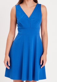 Robe bleue avec un corsage ajusté, un décolleté en V et une jupe évasée. Fabriquée en tissu lisse sans motifs visibles ni détails métalliques.