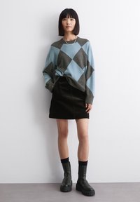 Hellblaues und graues Argyle-Pullover, schwarzer Cordrock und schwarze knöchelhohe Boots mit dicker Sohle, getragen mit dunklen Socken. Einfaches silbernes Kettenaccessoire.