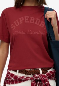 Rode katoenen t-shirt met korte mouwen, met een ronde halslijn en het logo "SUPERDRY Athletic Essentials" dat over de borst is gedrukt.