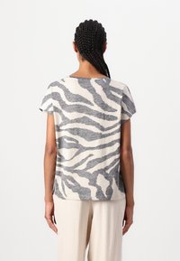 T-shirt à manches courtes en beige clair avec des rayures zèbres grises ; tissu doux et texturé ; coupe ample avec un ourlet droit et des épaules tombantes.