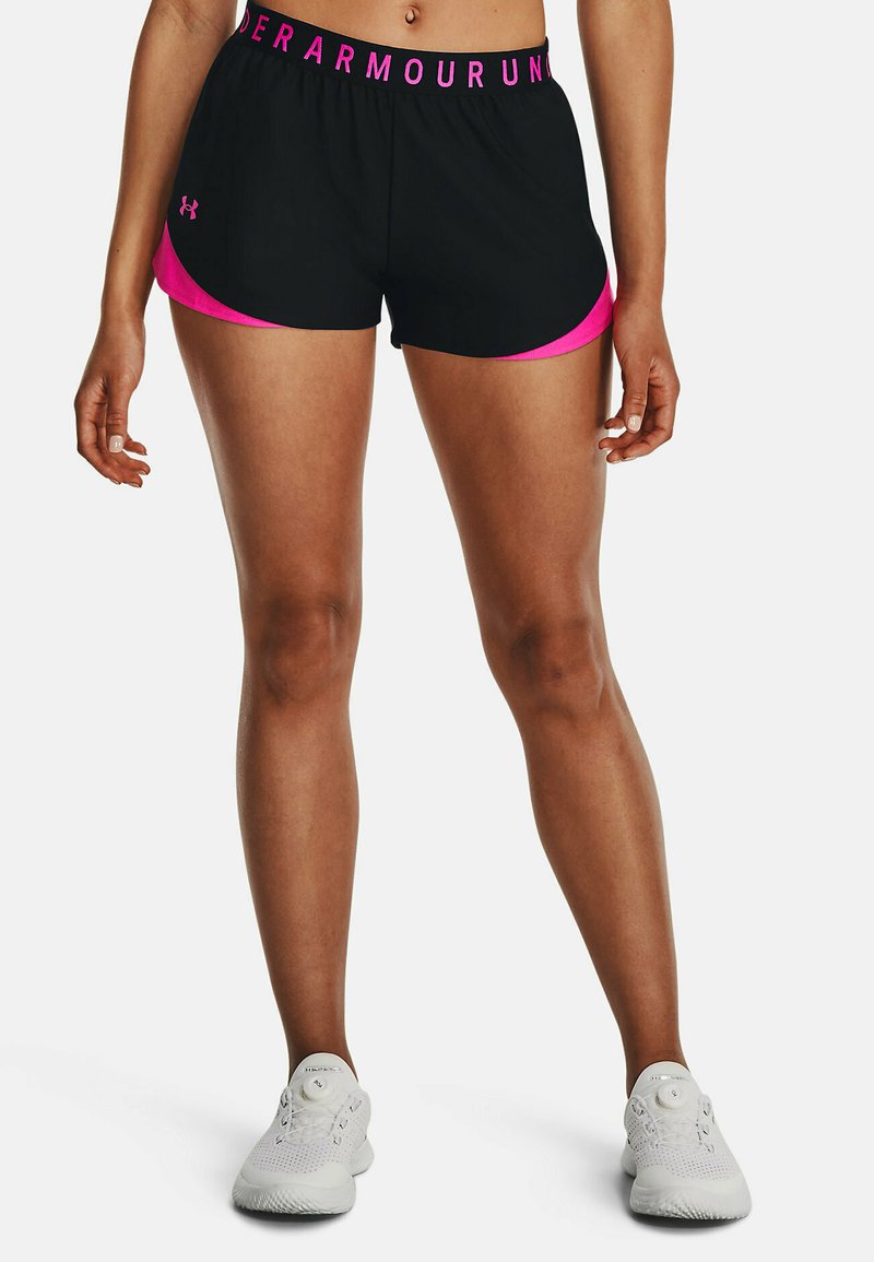 Pantalones cortos deportivos negros con acentos rosas. Cuentan con una cinturilla ancha con el texto "UNDER ARMOUR". Combinados con zapatillas blancas.
