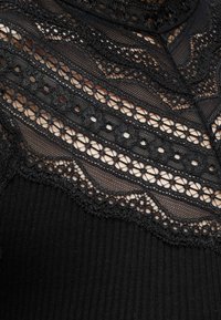 Material dantelă neagră cu modele florale și geometrice suprapuse peste un fundal textil negru cu textură nervurată.