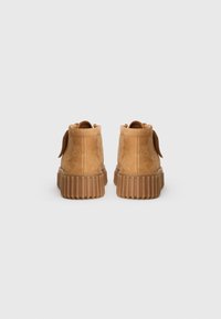 Tan suede ankle boots with a ridged rubber sole, rounded toe, and back loop for easy wear. Smooth texture with subtle stitching detail.