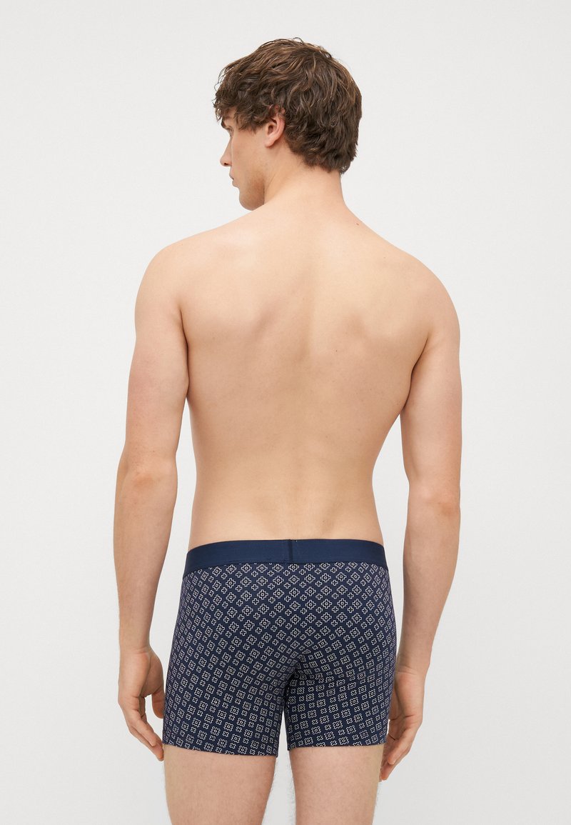 Navy blue patterned boxer shorts with a soft waistband and geometric design. Visible skin tone on the upper body and shoulders.