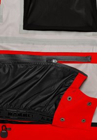 Rote und graue Jacke mit einem schwarzen Innenfutter. Verfügt über Reißverschlüsse und verstellbare Druckknöpfe. "MAMMUT" Branding auf der Innenseite. Texturiertes Material.