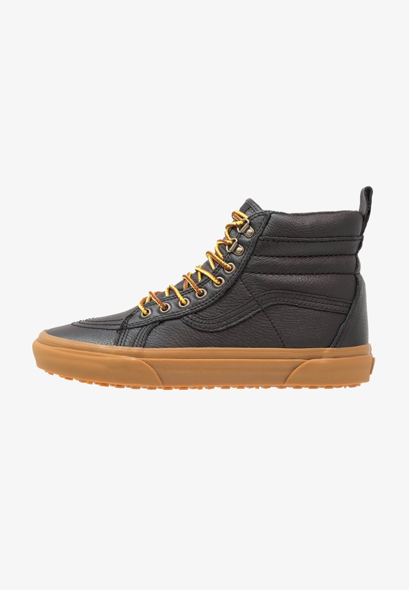 Sneaker montante en cuir noir avec col rembourré, lacets jaune-brun et semelle en caoutchouc épaisse marron, vue de côté.
