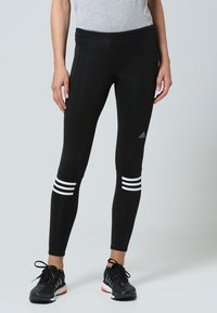 Svarta träningstights med hög midja, med tre vita horisontella ränder på varje vad och subtil logotypdetalj. Slät tygtextur.