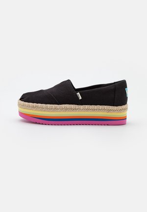 Zapato negro tipo slip-on de lona con plataforma de yute y multicolor, que presenta un borde trenzado y una suela de goma texturizada.