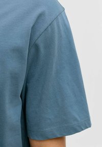 Camiseta de algodón azul claro con cuello redondo y mangas cortas. La tela tiene una textura suave con detalles sutiles de costuras.