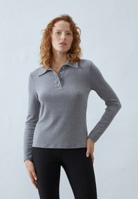 Grijze geribbelde lange mouw polo met een kraag, drie knopen en een slim fit silhouette. Draagt met zwarte leggings.