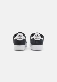 Zwarte suède sneakers met witte accenten, voorzien van een gevoerde kraag, textuur op de oppervlakte en een prominent logo op de hiel.