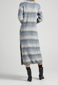 Abito lungo a righe in morbido tessuto peloso, con tonalità di blu, grigio e crema. Spacco laterale e colletto a costine. Indossato con stivali neri fino al ginocchio.
