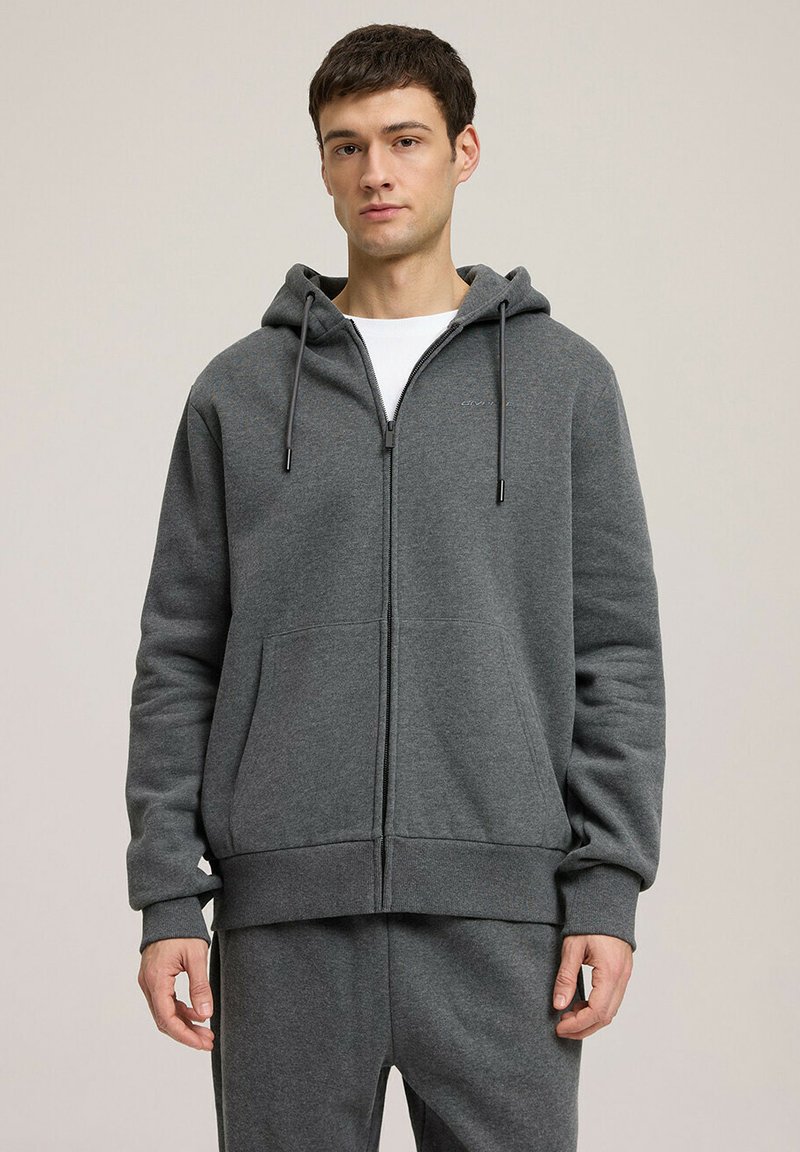 Szara bluza z kapturem na zamek, wykonana z miękkiego materiału, z kapturem ze sznurkiem, przednimi kieszeniami oraz ściągaczami przy mankietach i u dołu. Minimalistyczny design z detalem logo.