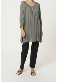 Blusa de manga larga gris con detalle de escote en forma de llavero y escote fruncido, combinada con pantalones negros de pierna recta y sandalias negras de tiras.