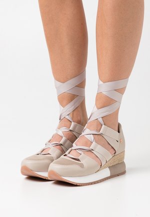 Zapatillas deportivas de cuña beige con tiras de cinta cruzadas, materiales de malla y cuero, superficie texturizada y suela de goma con un acento en blanco y marrón.