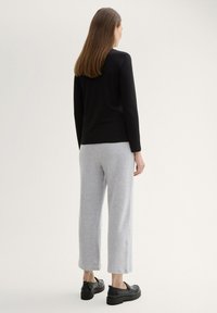 Top de manga larga negro de canalé combinado con pantalones de chándal gris de pierna ancha. La modelo lleva zapatos de plataforma negros. El fondo es neutral y sencillo.