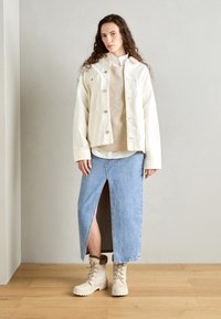 Hvit denimjakke med sølvknapper, beige ribbestrikket genser og blå denimskjørt med splitt foran. Høye beige snørestøvler med pels.