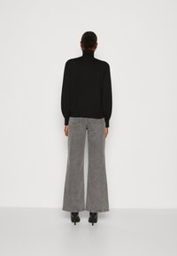 Schwarzer Rollkragenpullover mit langen puffärmel, kombiniert mit weit geschnittenen grauen Jeans. Das Model steht auf hochhackigen schwarzen Schuhen.