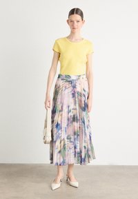 T-shirt ajusté jaune, jupe plissée avec un motif floral pastel, escarpins blancs à talon pointu et un léger sac à main. Tissu doux, longueur mi-mollet.