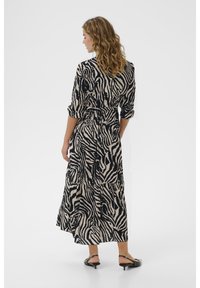 Maxiklänning i beige med svarta zebraränder, med bälte vid midjan, trekvartslånga ärmar och design med volanger.