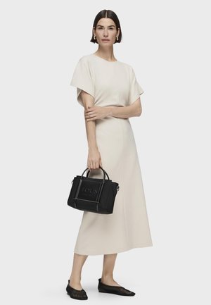 Abito midi beige chiaro con maniche corte, borsa a tracolla nera con logo "TOUS" e ballerine in rete nere. Materiale liscio e vestibilità comoda.