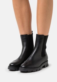 Svarta läderankelboots med elastiska sidopaneler, rund tå och texturerad gummisula med mönster.