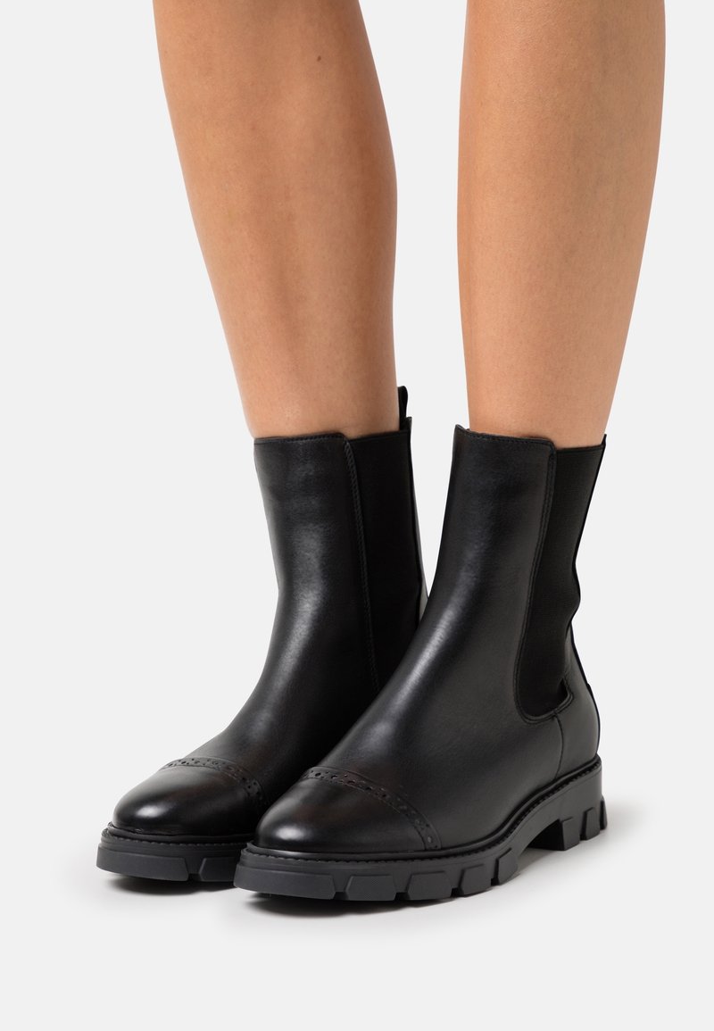 Svarta läderankelboots med elastiska sidopaneler, rund tå och texturerad gummisula med mönster.