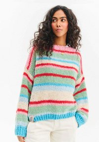 Wielokolorowy, gruby sweter dziergany w paski w kolorach czerwonym, niebieskim, zielonym i różowym. Mankiety i dół swetra wykończone ściągaczem, z małą naszywką z logo.