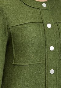 Green wool blend jacket with a collar, two front pockets, and silver snap buttons. Textured surface with a matte finish.