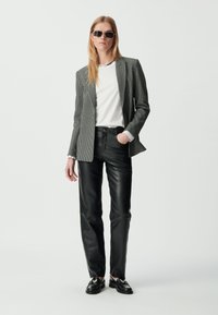 Czarny i biały kratkowany żakiet na białej koszuli, połączony z czarnymi skórzanymi spodniami z wysokim stanem i czarnymi mokasynami, tworzący zorganizowaną sylwetkę.