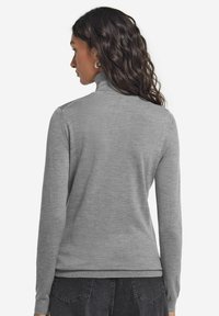 Grå långärmad polotröja tillverkad av mjukt stickat material, med slimmad passform och ribbade fållar. Bakifrån visar den en jämn textur och stil.