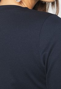 Top z bavlněného směsového materiálu tmavě modré barvy s kulatým výstřihem a krátkými rukávy, který se vyznačuje hladkou texturou a minimálním prošíváním.