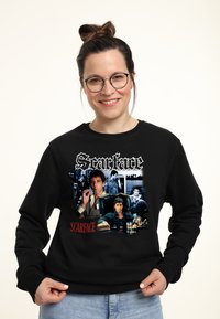Felpa nera con grafiche di "Scarface", assortimento di immagini dei personaggi e testo del titolo in bianco e rosso, mostrato in modo prominente sul davanti.